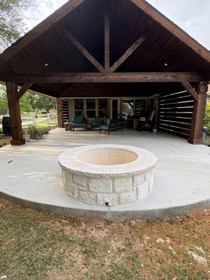 Stone fire pit on rounded concrete patio from inside the pavilion looking out